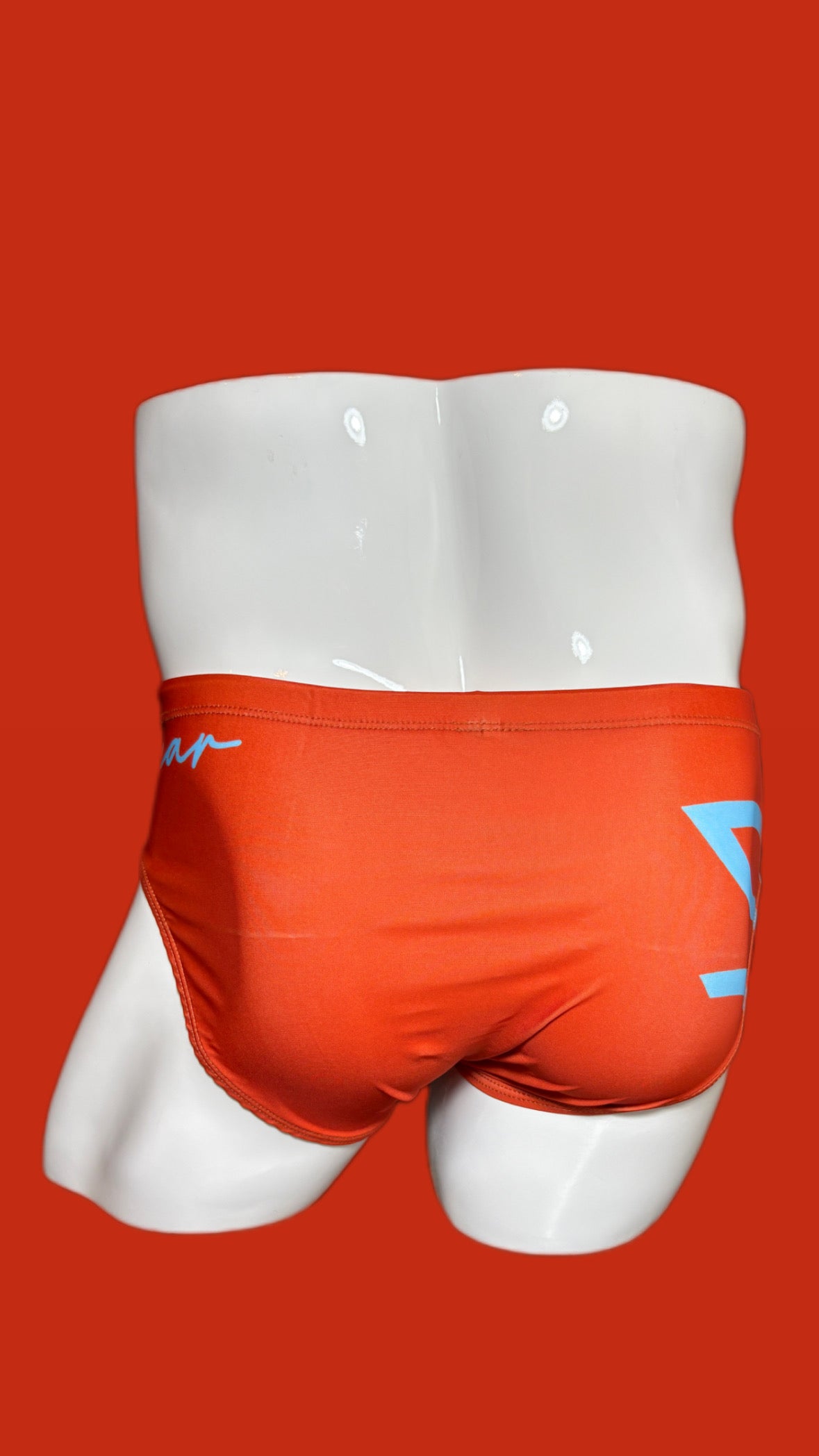 Orange swim briefs with a logo on a white mannequin against an orange background